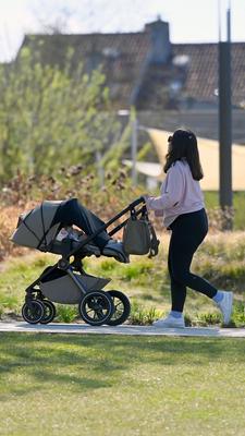 Eine Frau schiebt einen Kinderwagen auf einem Weg durch einen Park.
