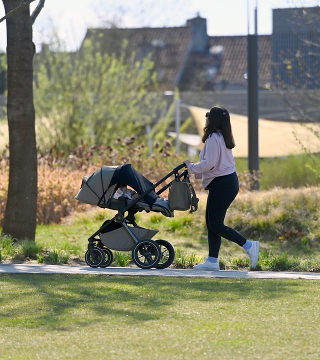 Eine Frau schiebt einen Kinderwagen auf einem Weg durch einen Park.