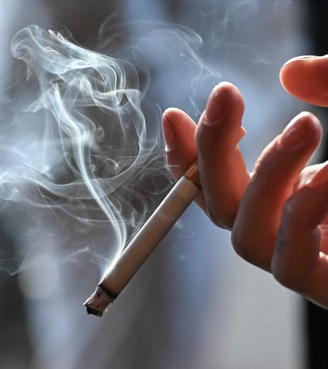 Ein Frau hält eine qualmende Zigarette in der Hand. 