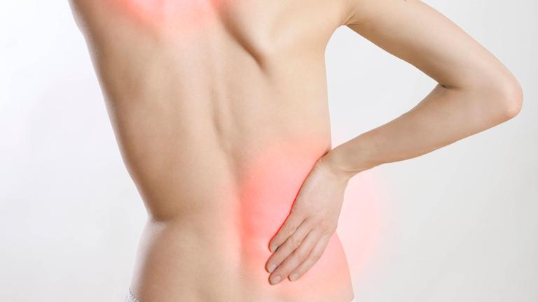 Eine Frau ist von hinten zu sehen. Sie greift sich mit den Händen in den Nacken und an den Rücken.