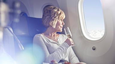 Eine Frau trinkt ein Glas Sekt im Flugzeug und blickt aus dem Fenster