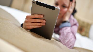 Frau liegt im Bett und schaut auf ihr Tablet
