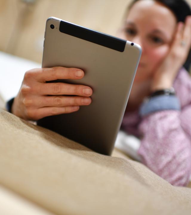 Frau liegt im Bett und schaut auf ihr Tablet
