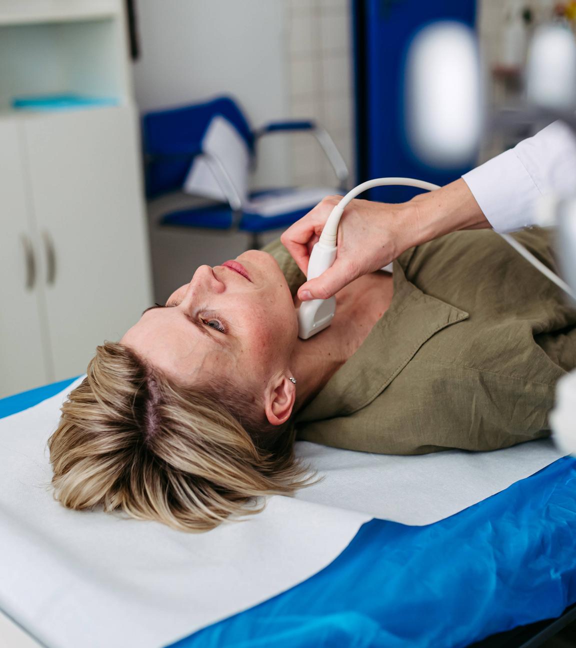 Eine Frau liegt auf einer Untersuchungsliege und erhält eine Ultraschalluntersuchung ihrer Schilddrüse.
