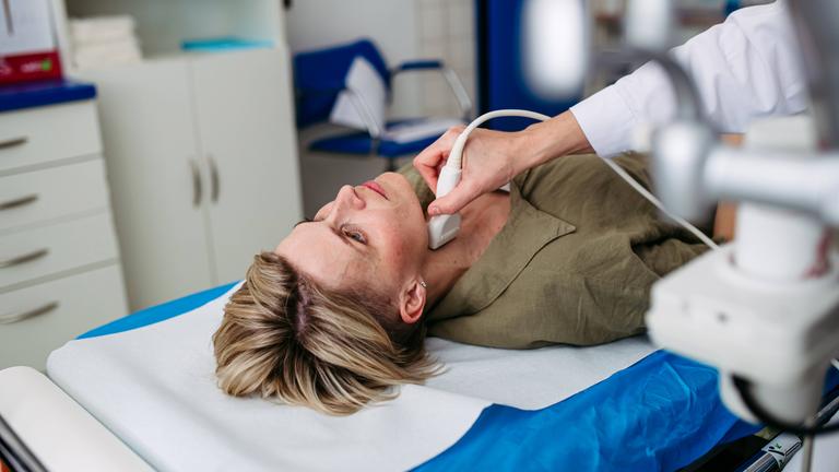 Eine Frau liegt auf einer Untersuchungsliege und erhält eine Ultraschalluntersuchung ihrer Schilddrüse.