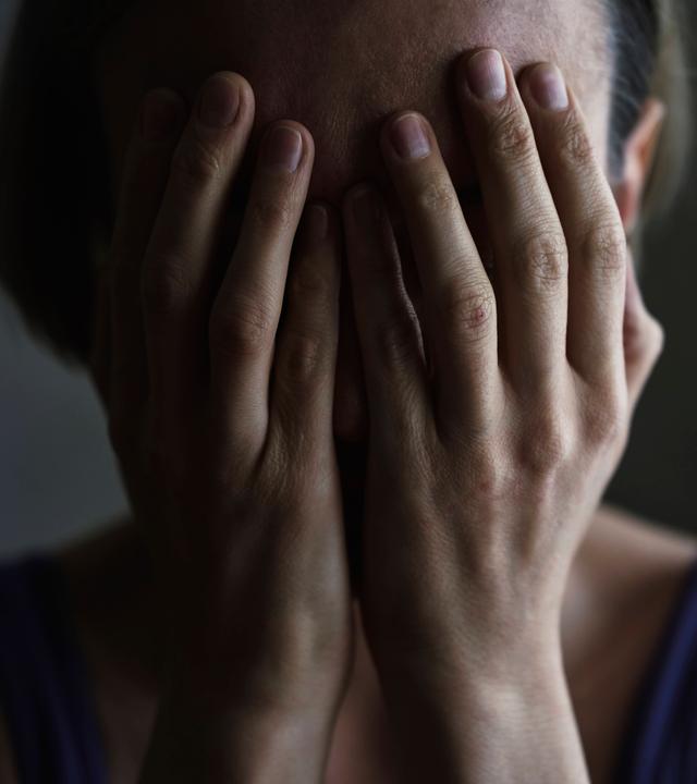 Eine Frau verdeckt mit ihren Händen ihr Gesicht.