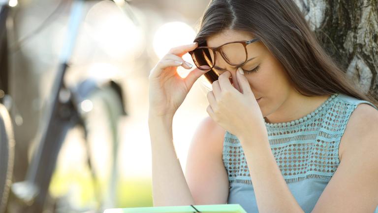 Frau schiebt sich die Brille hoch und greift mit einer Hand an ihre Nase.