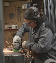 Die Ofenbauerin Laura Hack geht ihrer handwerklichen Tätigkeit nach. Sie trägt Schutzklamotten und eine Schutzbrille.