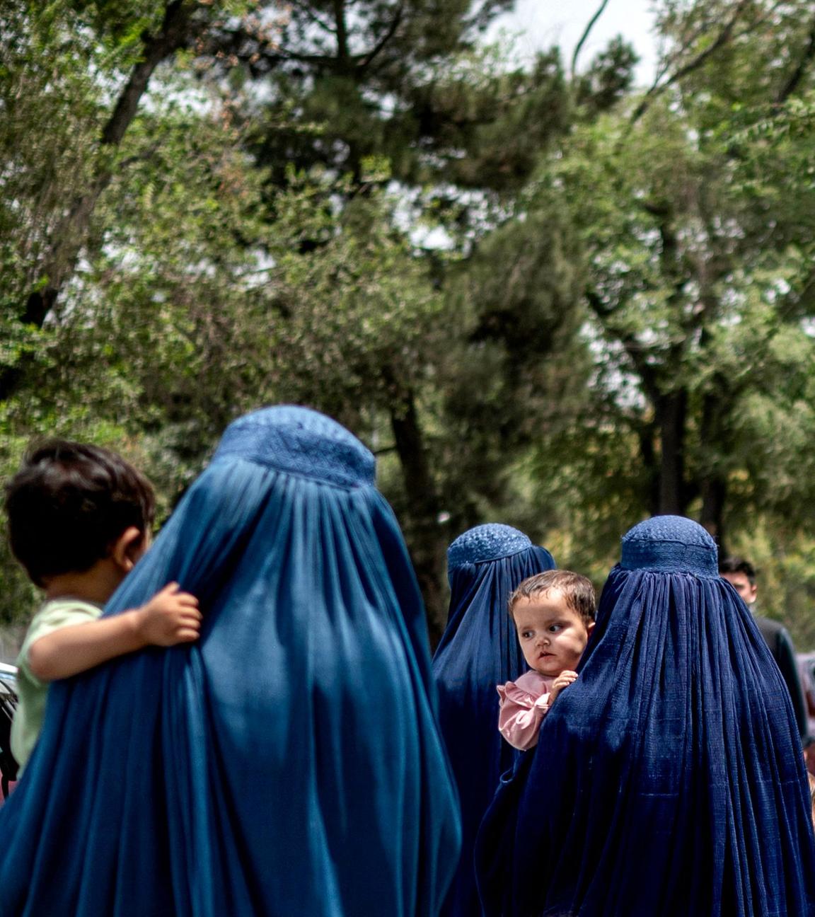 Afghanische Frauen in Burkas gehen am Vorabend des vierten Jahrestages der Machtübernahme der Taliban im Jahr 2021 am 14. 8. 2025 in Kabul an Taliban-Flaggen vorbei. 