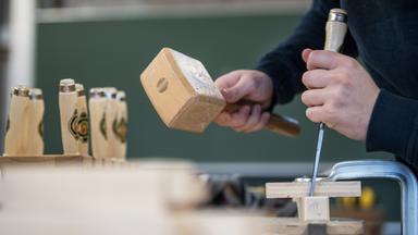 Ein Auszubildender im Handwerk arbeitet an einer Werkbank mit Holz.