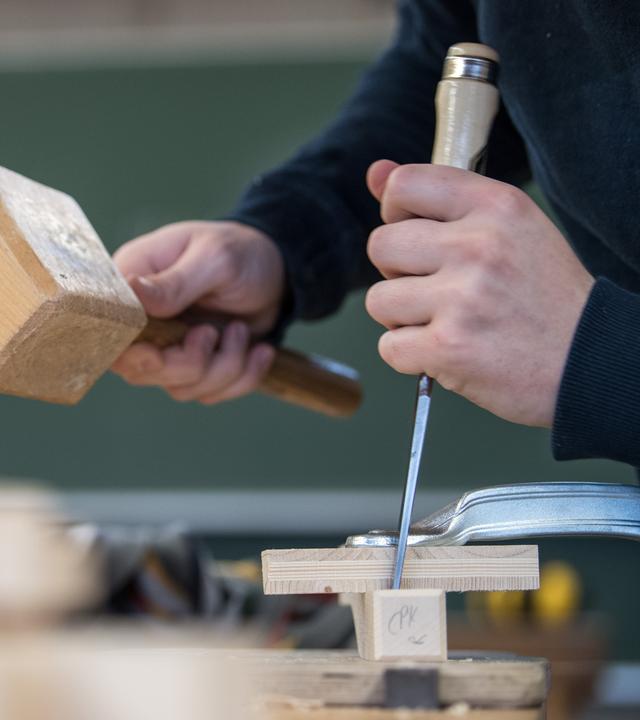 Ein Auszubildender im Handwerk arbeitet an einer Werkbank mit Holz.