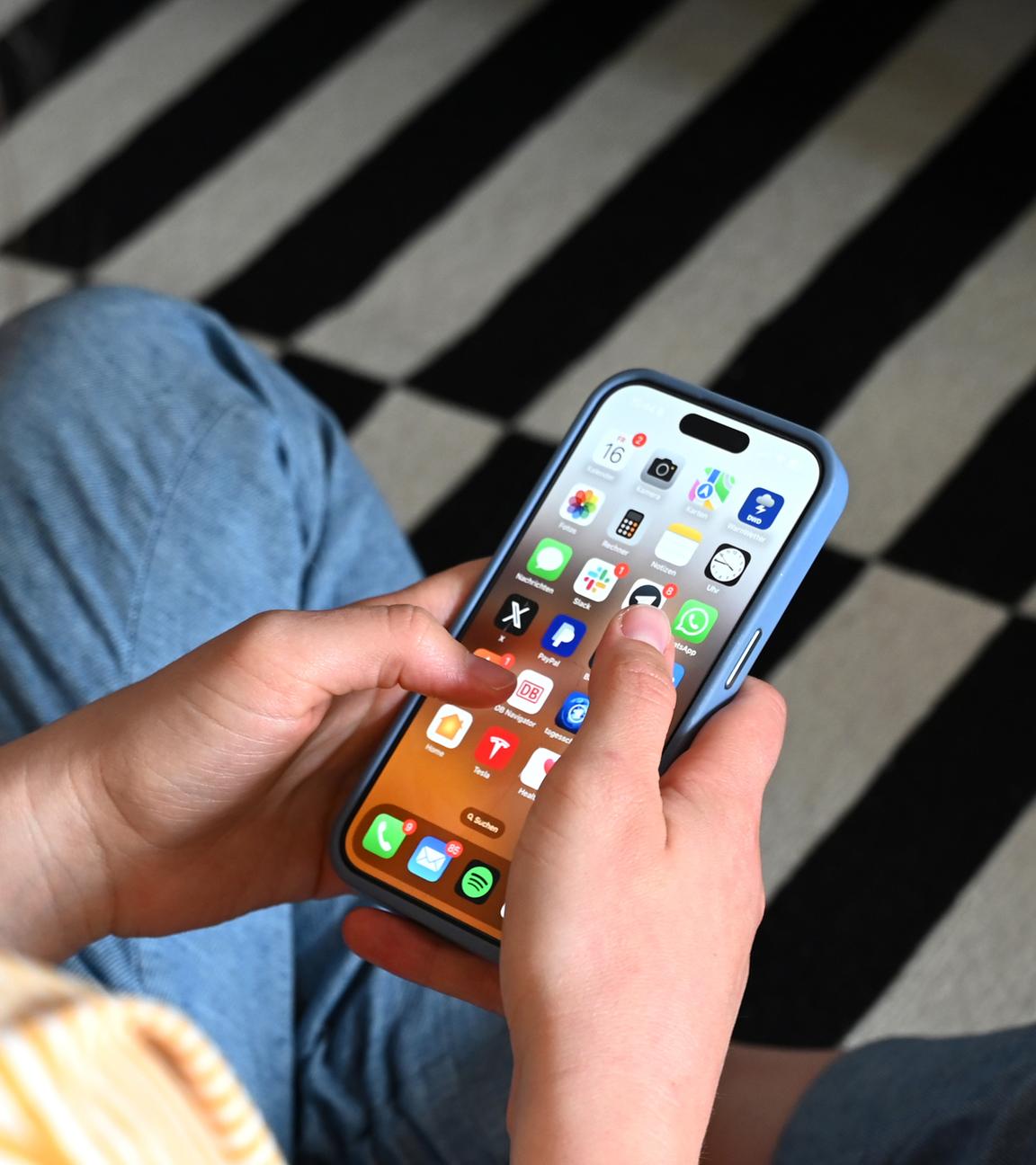 17.05.2025, Sachsen, Leipzig: Eine Jugendliche sitzt auf dem Boden und nutzt ein Smartphone - auf dem Display sind verschiedene Apps zu sehen.