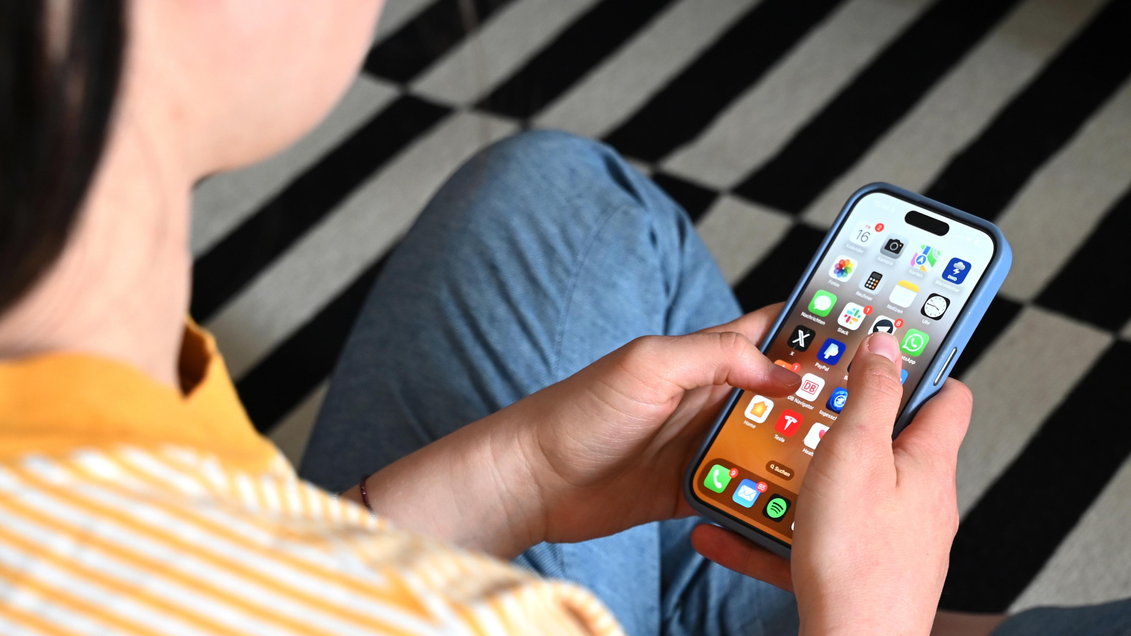 17.05.2025, Sachsen, Leipzig: Eine Jugendliche sitzt auf dem Boden und nutzt ein Smartphone - auf dem Display sind verschiedene Apps zu sehen.