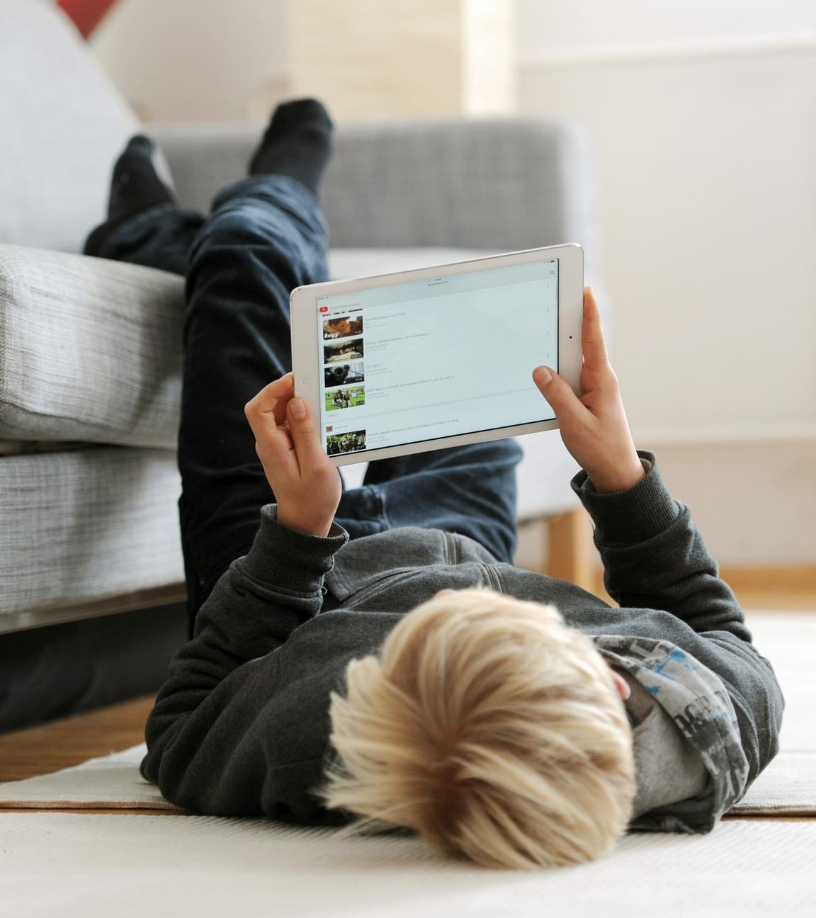 ein jugendlicher liegt gemuetlich auf dem fussboden und betrachtet die video-plattform "youtube" auf seinem ipad, aufgenommen am 09.12.2014 in muenchen (bayern).