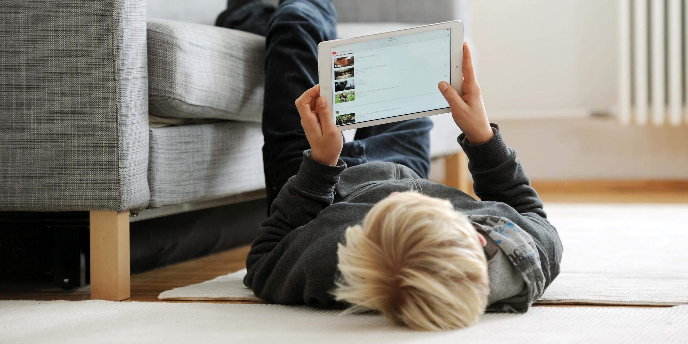 ein jugendlicher liegt gemuetlich auf dem fussboden und betrachtet die video-plattform "youtube" auf seinem ipad, aufgenommen am 09.12.2014 in muenchen (bayern).