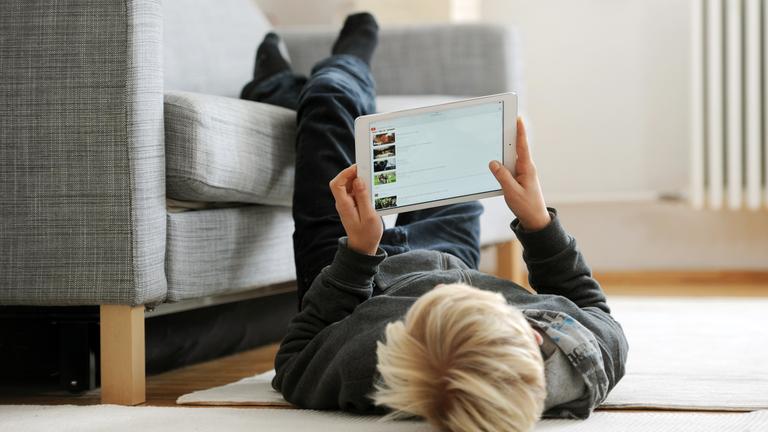 ein jugendlicher liegt gemuetlich auf dem fussboden und betrachtet die video-plattform "youtube" auf seinem ipad, aufgenommen am 09.12.2014 in muenchen (bayern).