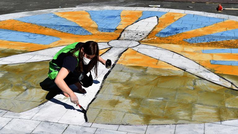 Eine Fridays for Future-Aktivistin malt ein Windkraftrad vor Sonne auf den Boden