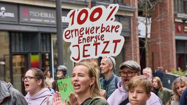Ein Teilnehmer auf einer Demonstration für die Energiewende hält auf der Mönckebergstraße ein Transparent mit der Aufschrift "100% erneuerbare Ernergie jetzt". 