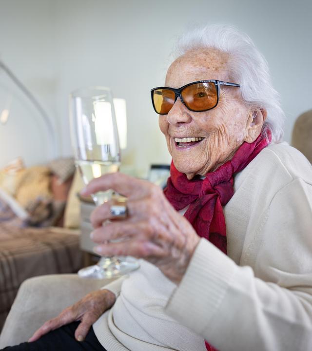 Friedel Zimmermann hält ein Glas mit Sekt in die Höhe und lächelt dabei.
