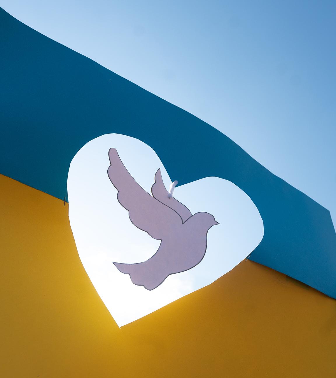 Eine Taube aus Papier schwebt in einer Ukraineflagge aus Papier. 