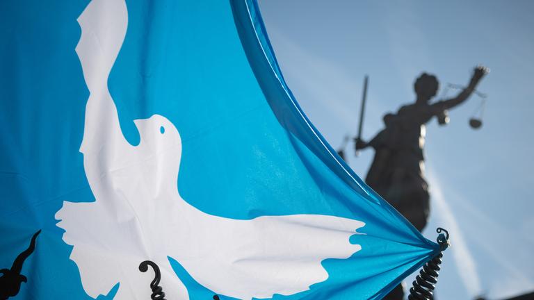 Eine Fahne mit einer Friedenstaube weht vor der Statue der Justitia.