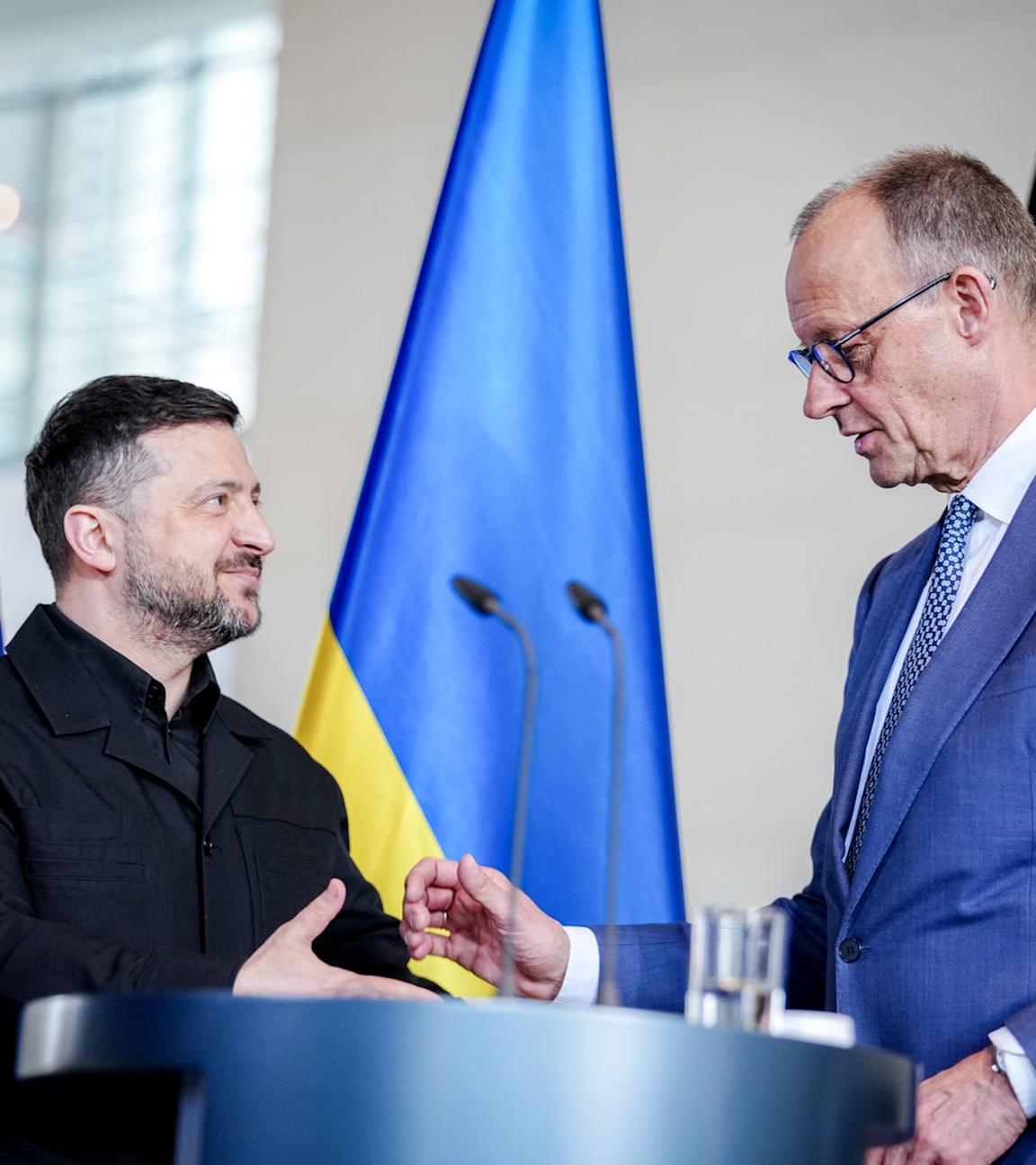 Bundeskanzler Friedrich Merz und Wolodymyr Selenskyj, Präsident der Ukraine, geben im Bundeskanzleramt bei den deutsch-ukrainischen Regierungskonsultationen eine Pressekonferenz. Sie stehen vor einem Mikrofon-Pult und sind im Begriff sich die Hände zu geben.