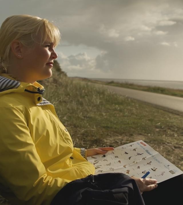 Marina Wenk sitzt auf einer Bank am Wegesrand in Friesland in den Niederlanden. Die Sonne scheint aufs Wasser.