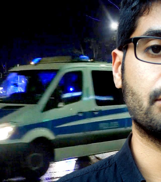 Journalist Mohamed Amjahid (Vordergrund), Polizei-Mannschaftswagen (Hintergrund)