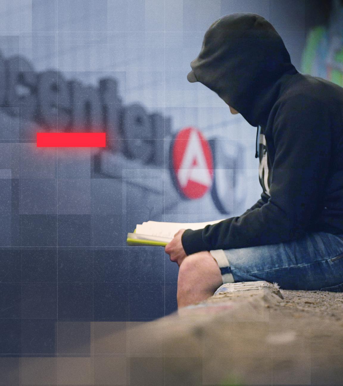 Mann mit schwarzem Hoodie sitzt vor einem Gebäude mit "jobcenter"-Schriftzug