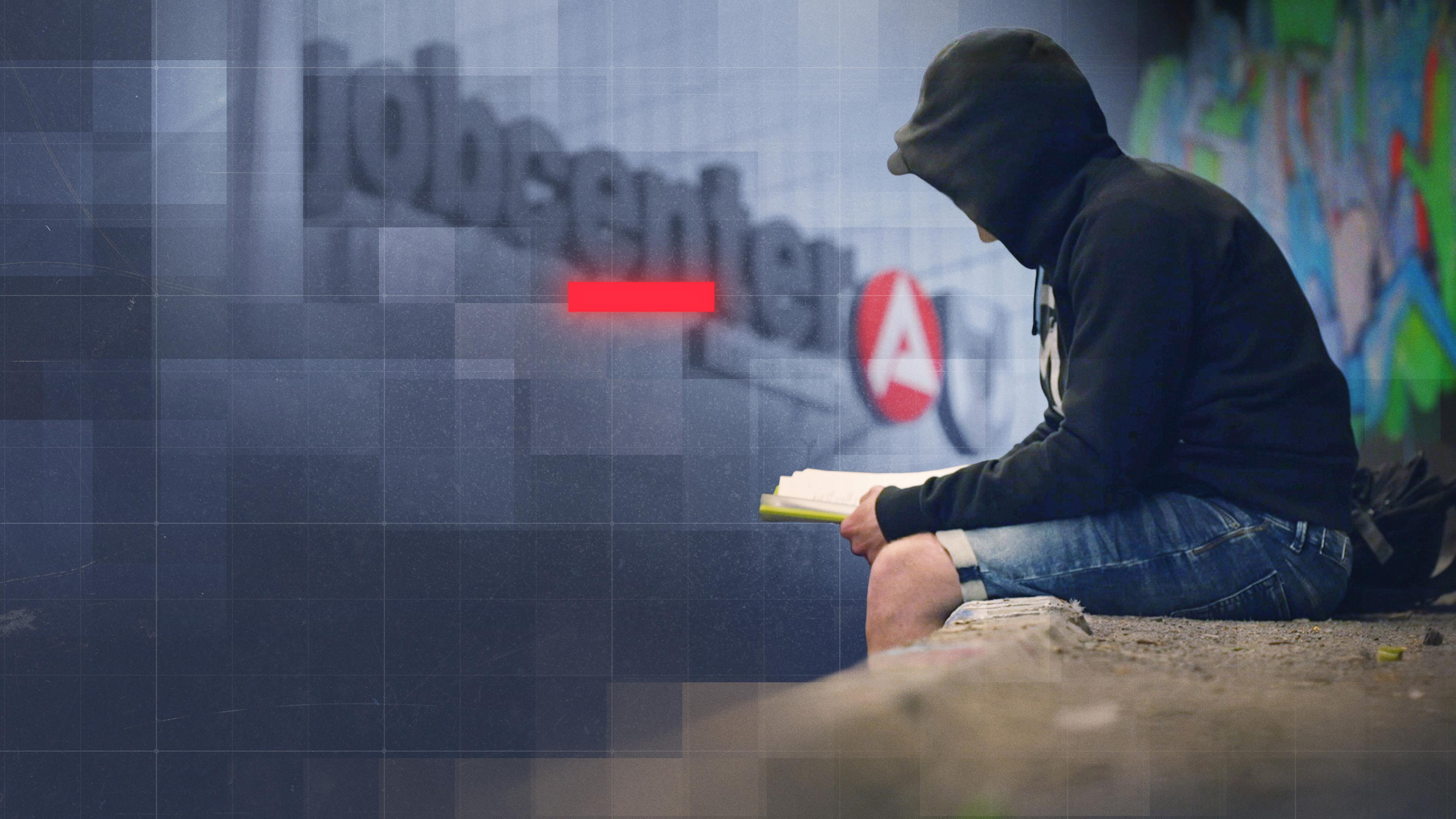 Mann mit schwarzem Hoodie sitzt vor einem Gebäude mit "jobcenter"-Schriftzug