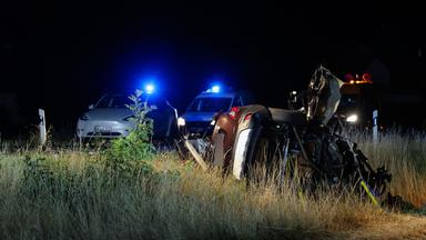 Ein vom Unfall beschädigtes Auto und zwei Polizeiwagen. 