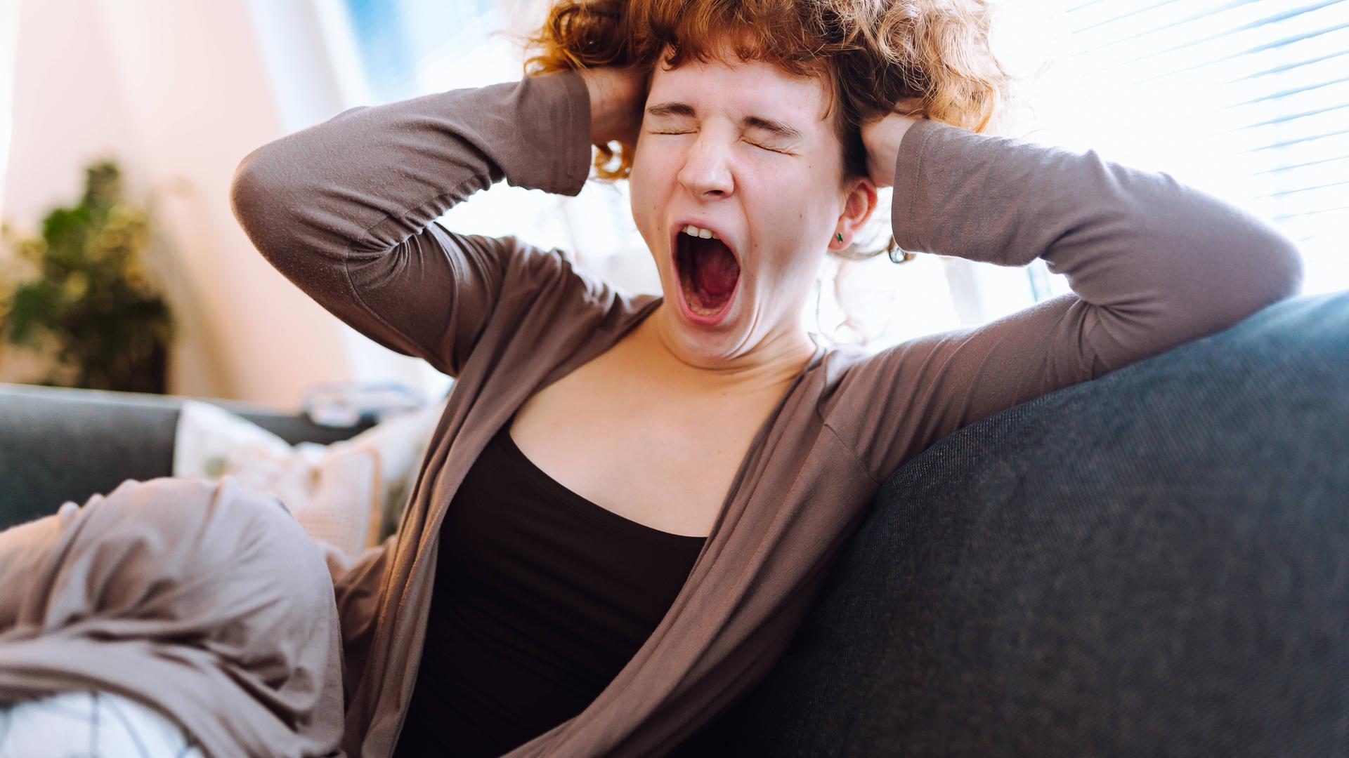Ein junge Frau sitzt auf dem Sofa und gähnt.