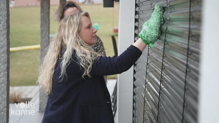 Eine Frau putzt mit einem Lappen die Raffstores von außen.