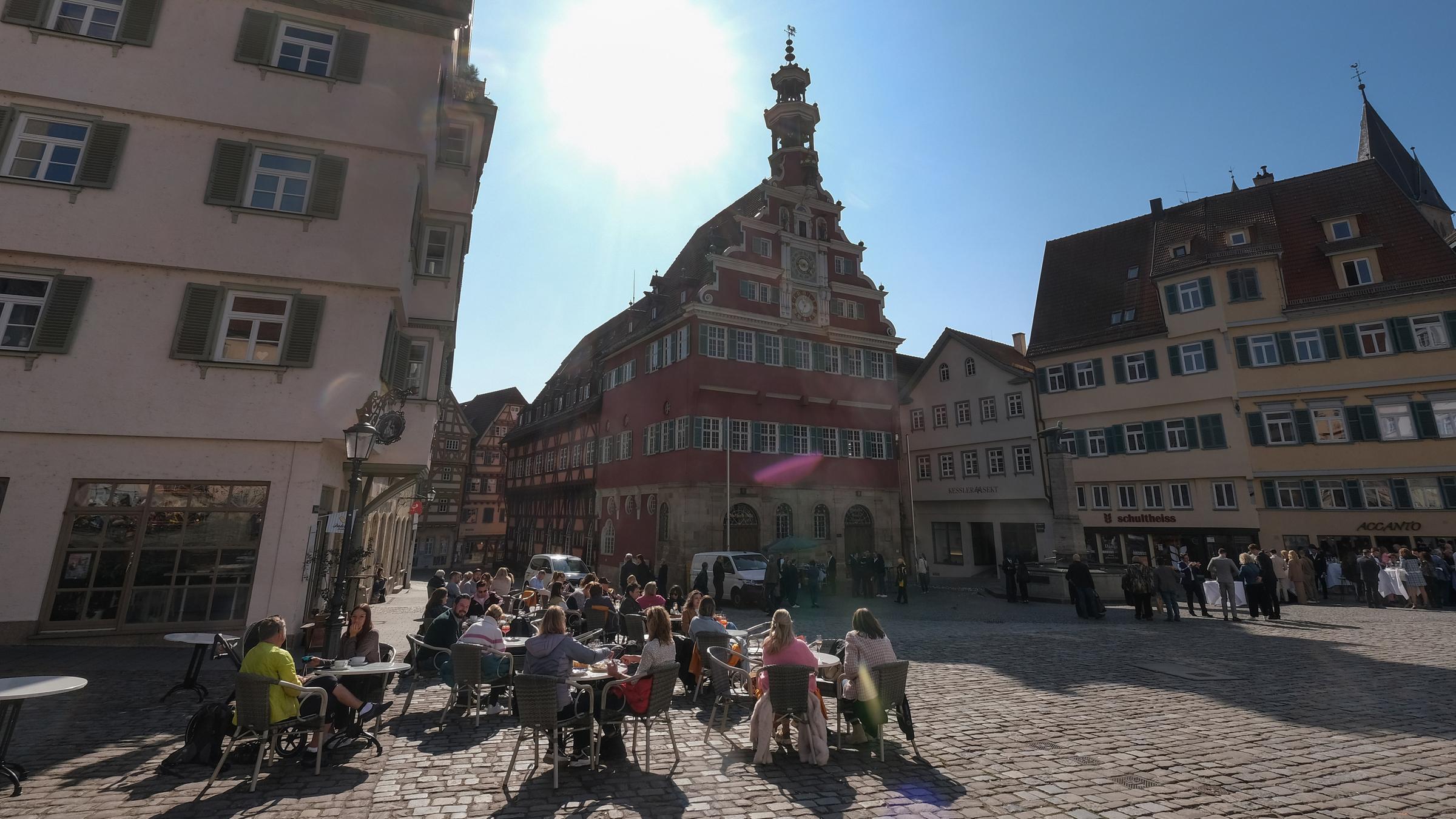 Baden-Württemberg, Eßlingen: Die strahlende Sonne steht am Himmel über dem Esslinger Rathaus, vor dem Passanten in einer Außengastronomie bei frühlingshaften Temperaturen sitzen.
