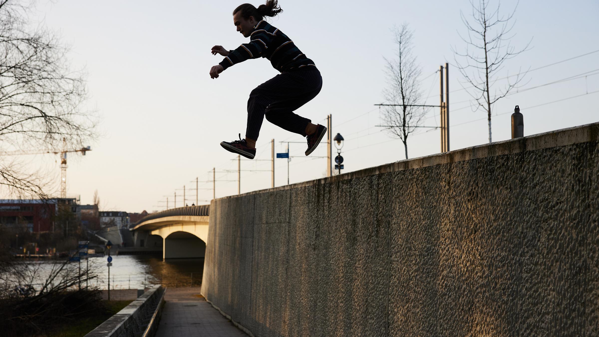 Brandenburg, Potsdam: Parcours-Sportler Niels springt bei Sonnenschein von einer Mauer nahe der Humboldtbrücke.