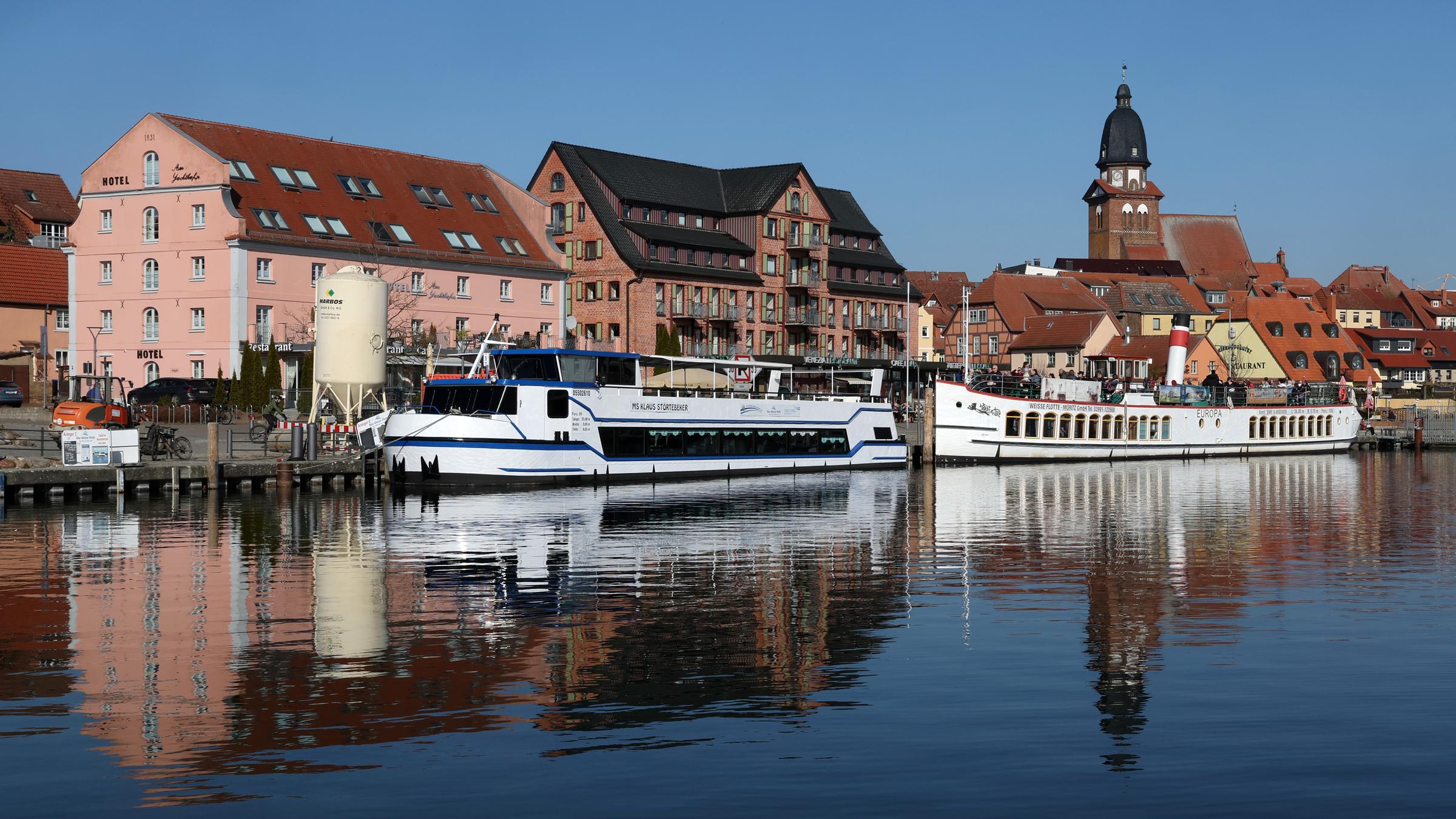 Mecklenburg-Vorpommern, Waren (Müritz): Im Stadthafen an der Müritz liegen bei sonnigem Frühlingswetter die Ausflugsschiffe für Rundfahrten bereit, sie spiegeln sich mit der Silhouette der Marienkirche und  der Stadt im ruhigen Wasser.
