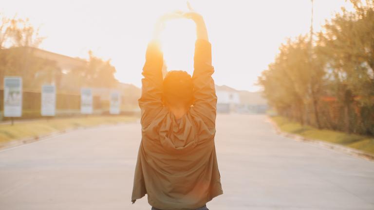 Ein Jogger, den man von hinten sieht, führt Dehnungsübungen im Sonnenaufgang durch.