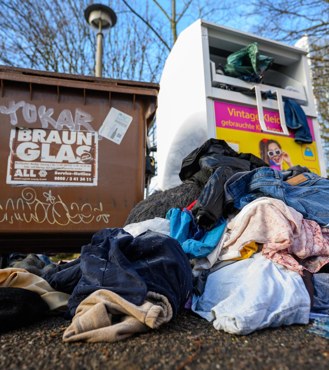 Ein überfüllter Altkleider-Container. Vor dem Container liegen bereits einige Müllsäcke mit Kleidung, die nicht mehr in den Container gepasst haben.