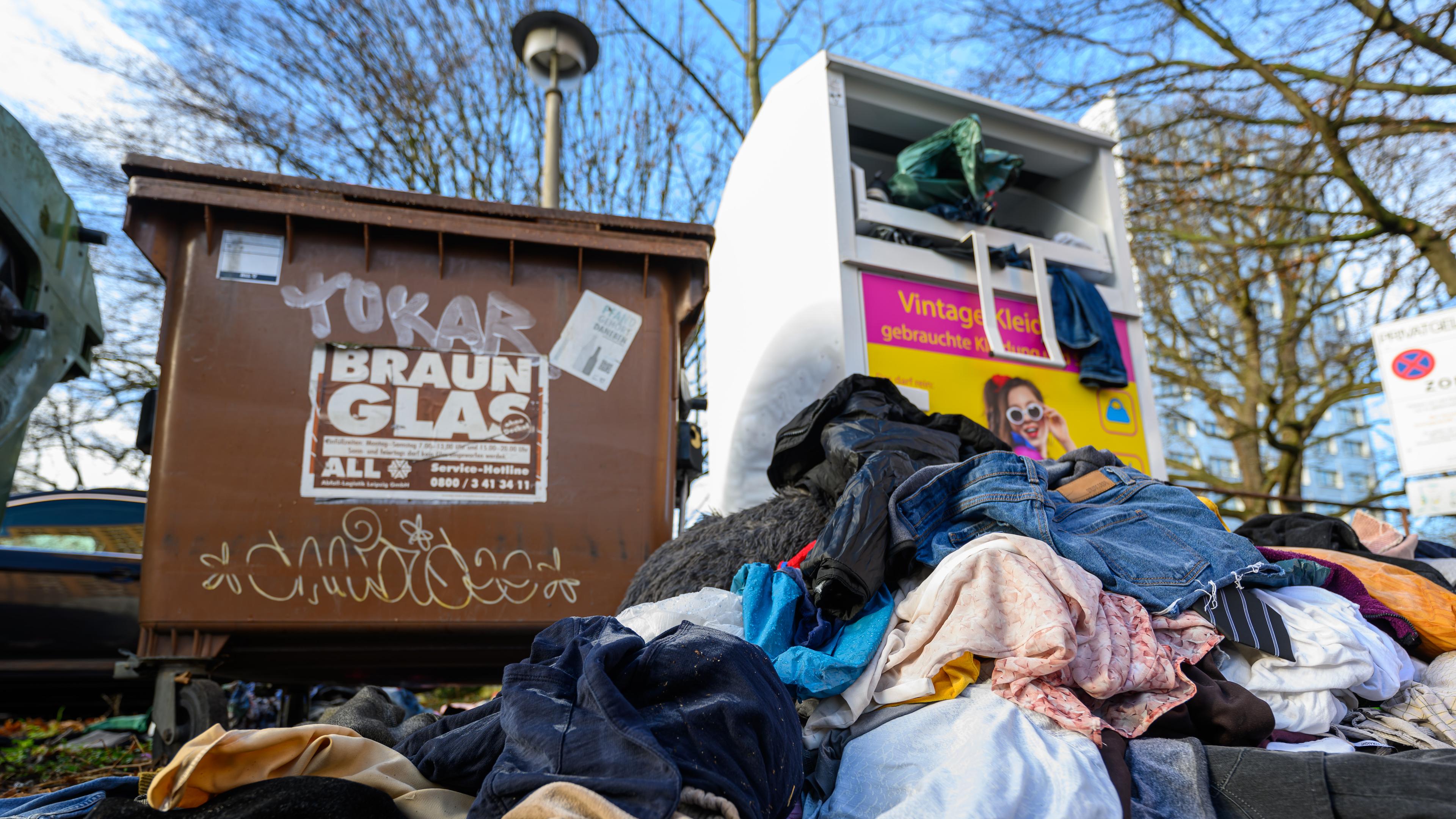 Ein überfüllter Altkleider-Container. Vor dem Container liegen bereits einige Müllsäcke mit Kleidung, die nicht mehr in den Container gepasst haben.