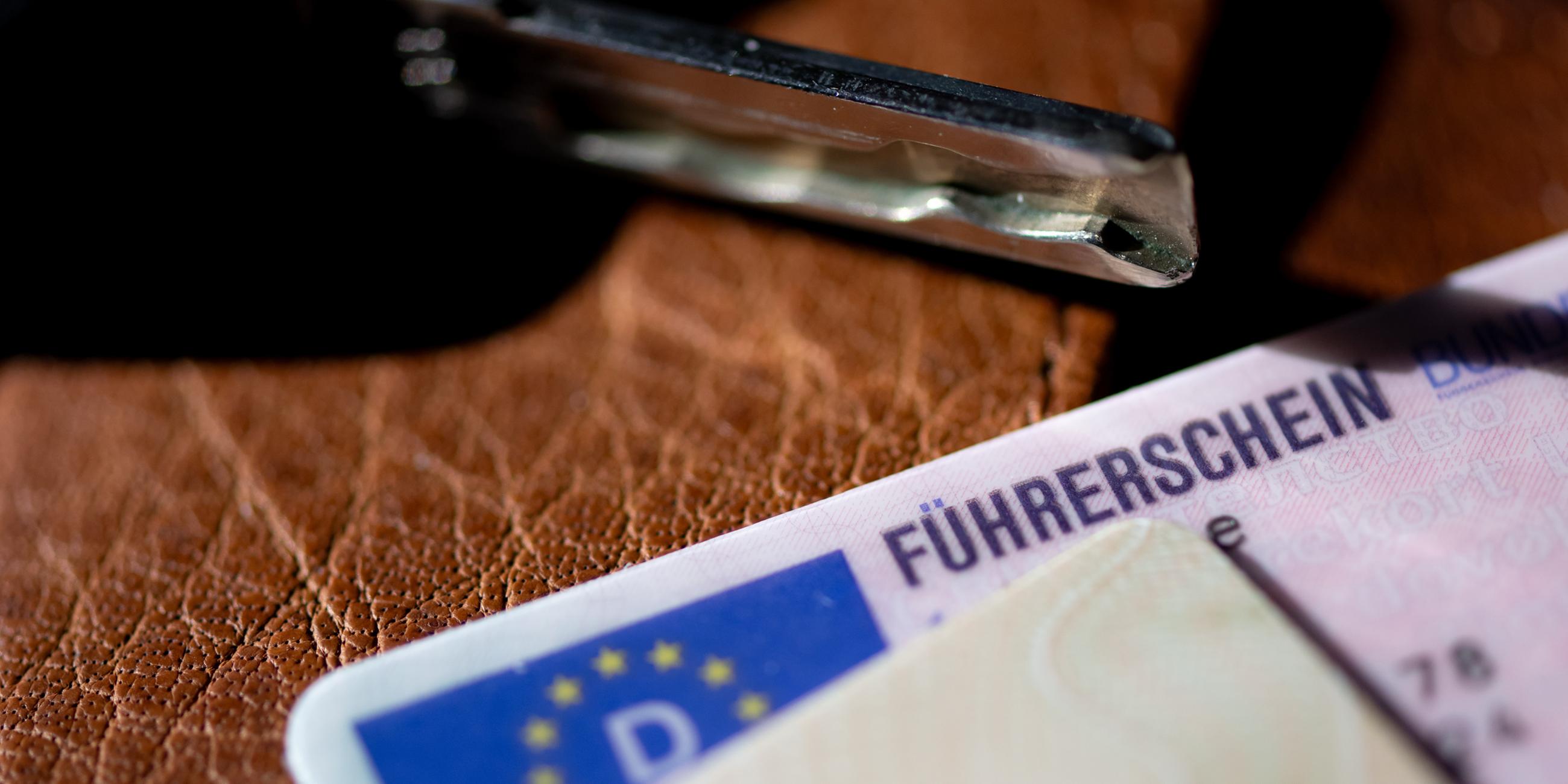 Ein Führerschein, ein Autoschlüssel und ein Personalausweis liegen auf einem Portemonnaie.