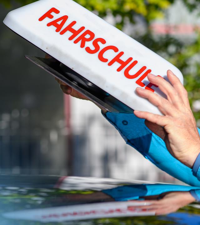Das Dach eines Fahrschulautos, auf dem das "Fahrschule"-Schild gerade platziert wird