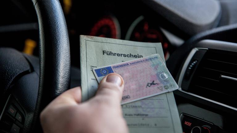 Ein Mann im Auto hält einen Papierführerschein und einen Führerschein im Scheckkartenformat in der Hand.