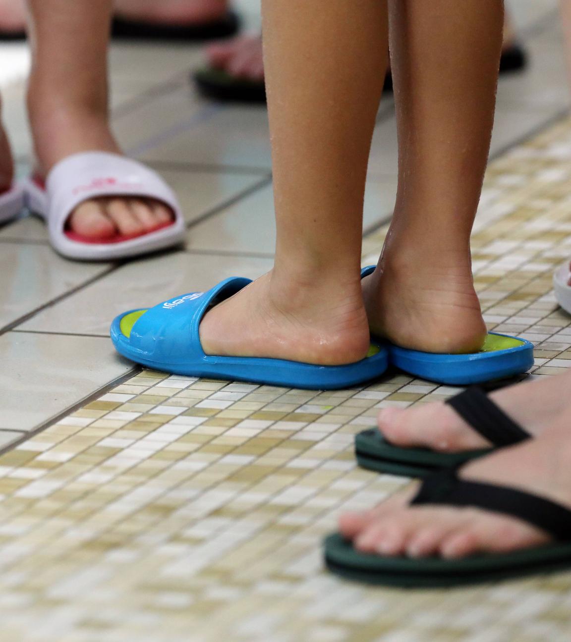 Mehrere Füße in Badeschuhen in einem Schwimmbad.