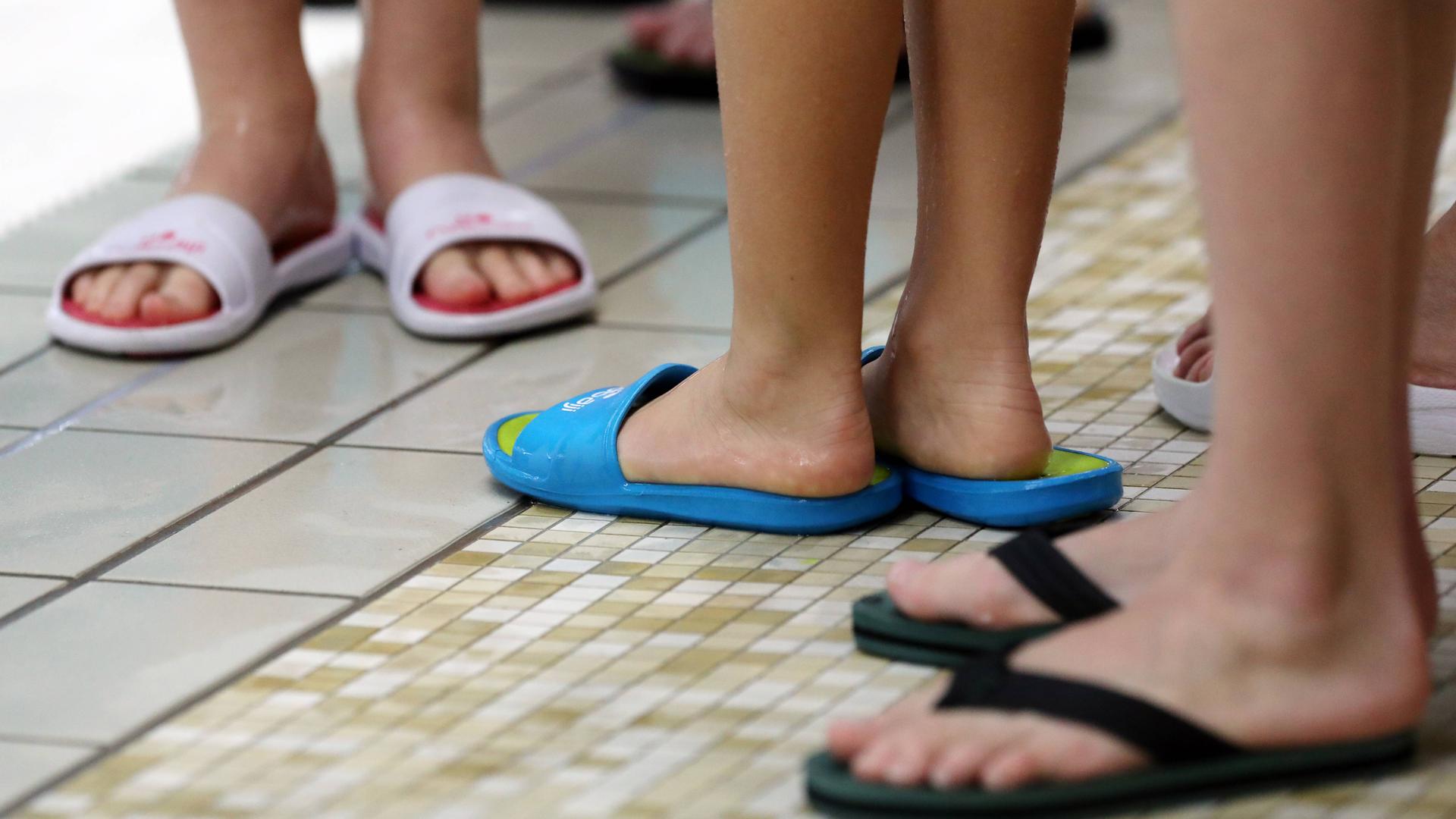 Mehrere Füße in Badeschuhen in einem Schwimmbad.