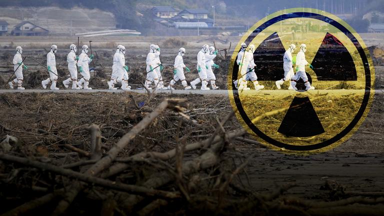 Mehrere Männer in Strahlenschutzanzügen gehen auf einer Straße, im Vordergrund Schutt. Rechts im Bild das Symbol für Radioaktivität.