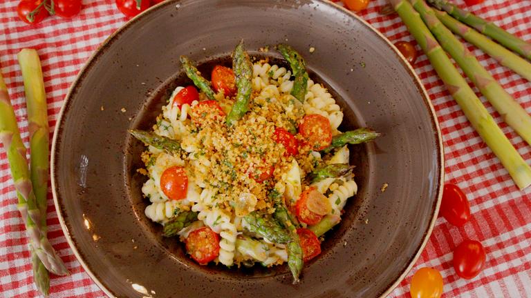 Fusilli verfeinert mit grünem Spargel auf einem dunklen Teller angerichtet