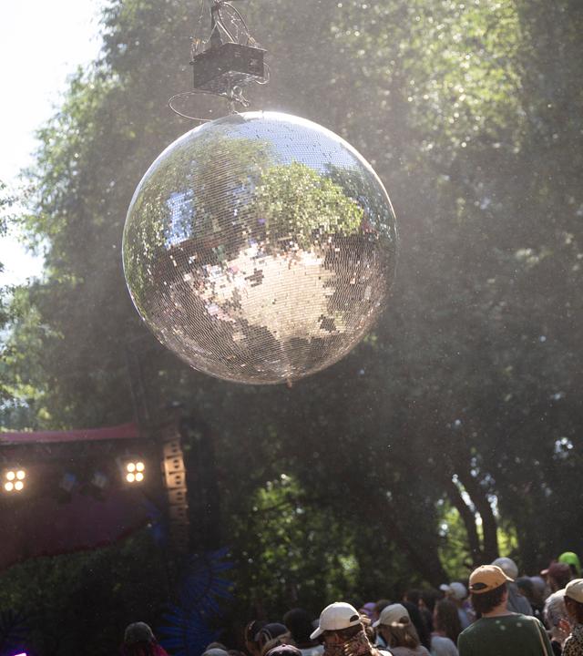 Eine Discokugel, unter der im Freien Menschen tanzen.