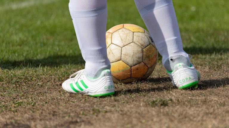 Ein Fussball liegt auf ausgetrocknetem Rasen. 