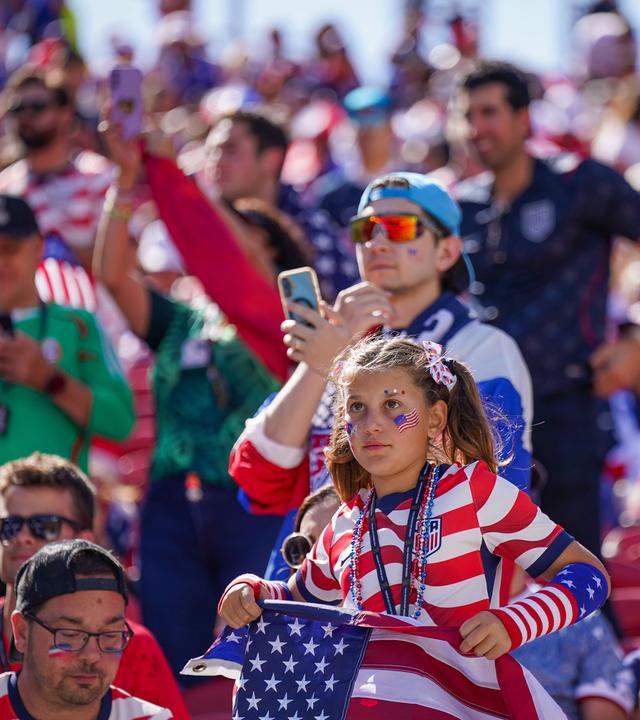 Mädchen im USA-Trikot mit Flagge und Gesichtsbemalung verfolgt das WM-2026-Spiel gegen Bosnien-Herzegowina auf der Tribüne.