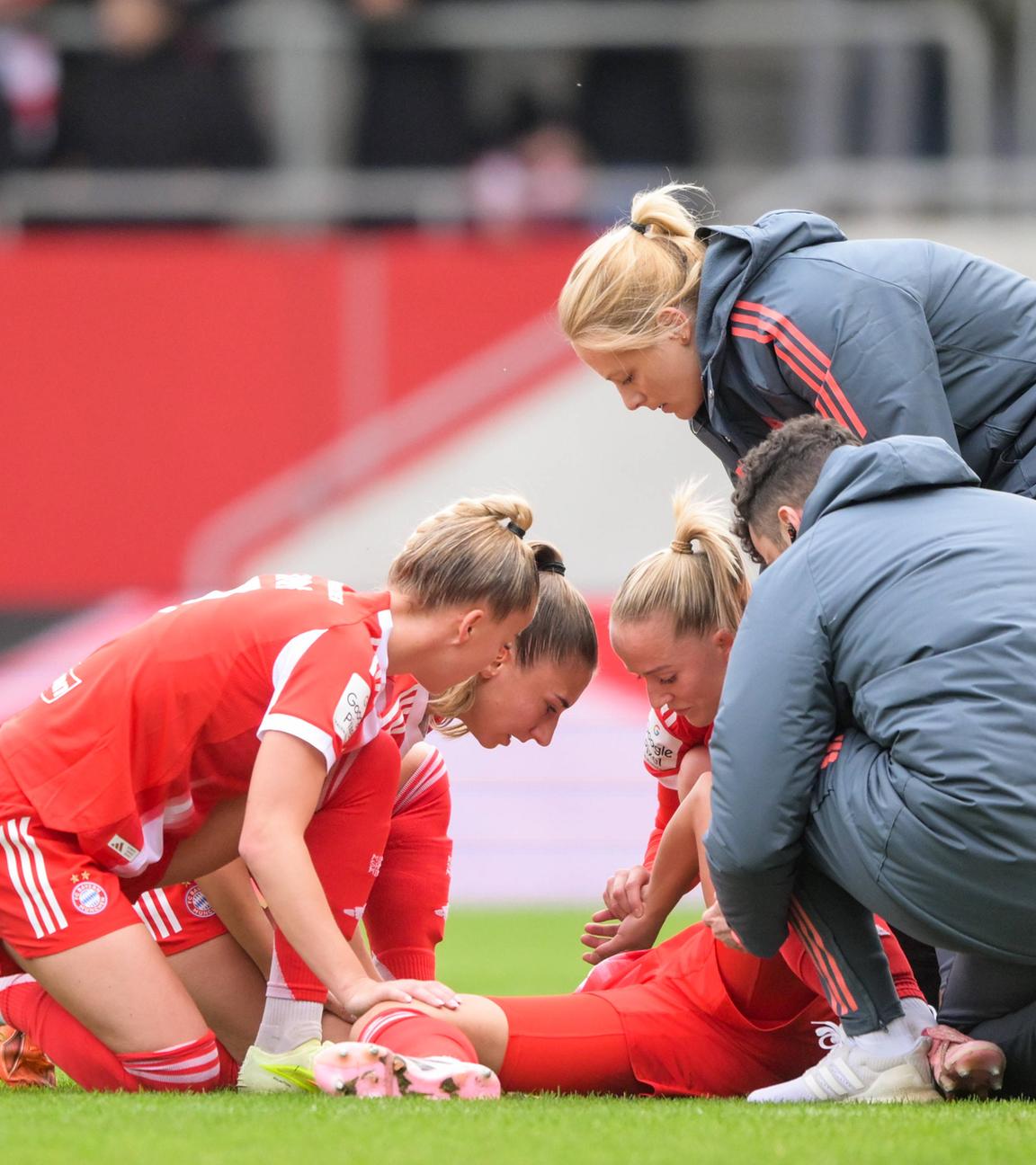 Fußballerin Lena Oberdorf liegt auf dem Spielfeldbogen, umgeben von besorgten Kolleginnen und einem Kollege, nachdem sie sich während einem Spiel verletzte.